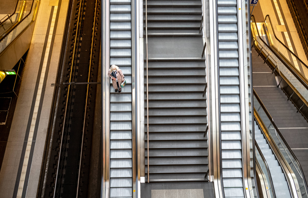 An older woman with a face mask taking an escalator at the almost empty main train station in Berlin during the Coronavirus pandemic.
