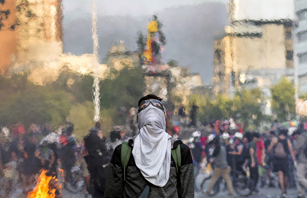 A hooded protester dries his clothes next to a barricade in downtown Santiago, with the statue of Plaza Baquedano in the background. When 40 days of social demonstrations have passed in the country.
