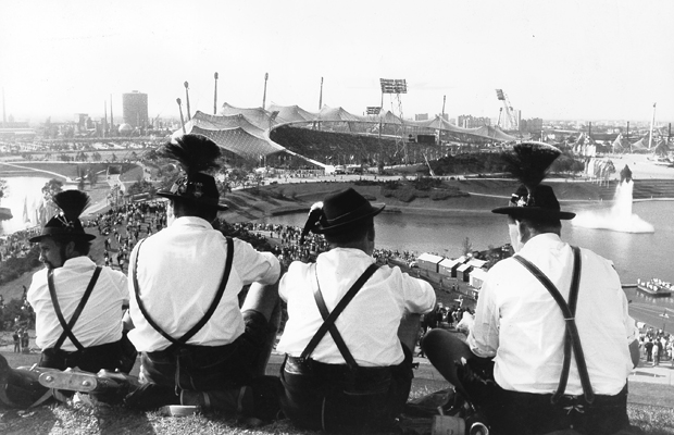 Zuschauer in bayerischer Tracht blicken vom Olympiaberg auf das Olympiastadion.